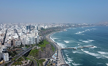 Vista aérea de la Costa Verde en Lima, con edificios frente al mar y olas del océano Pacífico